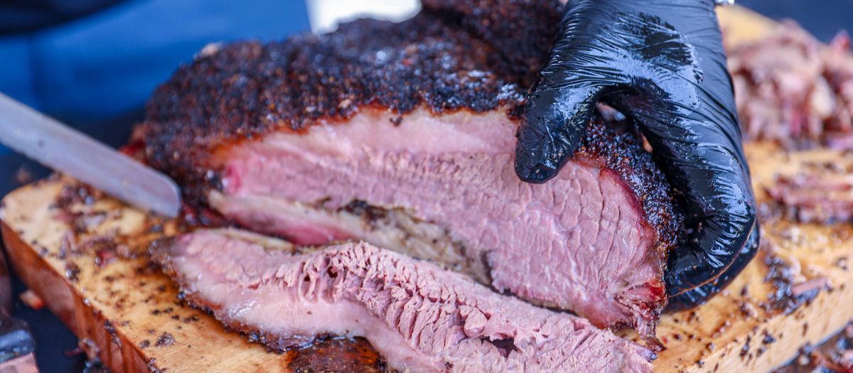 A brisket smoking on a pellet grill with thin blue smoke rising.