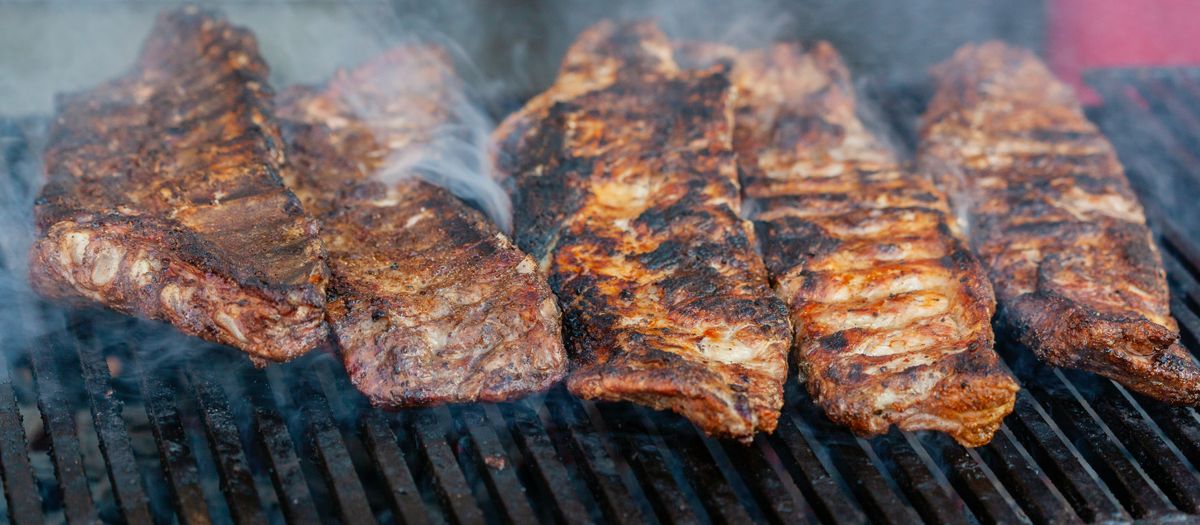 Close-up of delicious grilled ribs smoking on a barbecue grill, perfect for a summer cookout.