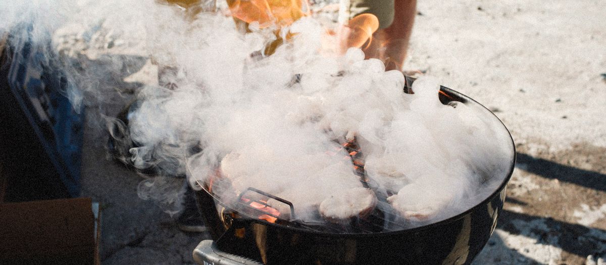 Grilling meat on a smoky barbecue grill outdoors on a sunny day.