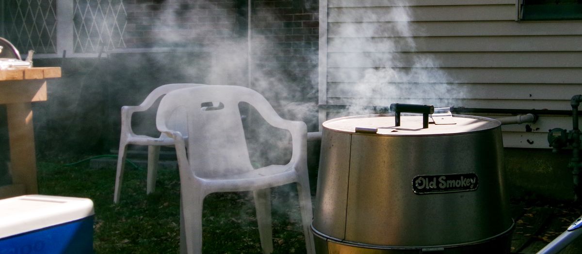 Smoke rising from a barbecue grill beside empty chairs in a Houston backyard setting.